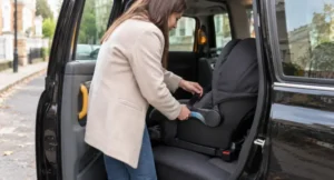 Parent fitting a rear-facing baby car seat on the back seat of a black cab